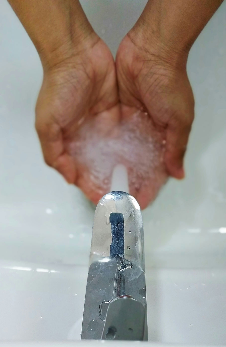 Personne blanche en train de se laver les mains sous un robinet en inox